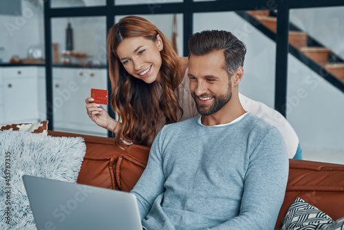 Happy young couple using laptop and smiling while shopping online at home