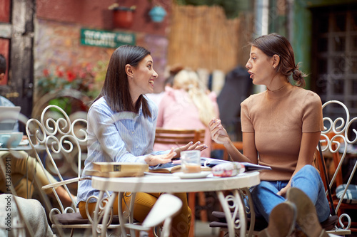Two female students chatting while have a drink in bar's garden. Leisure, bar, friendship, outdoor