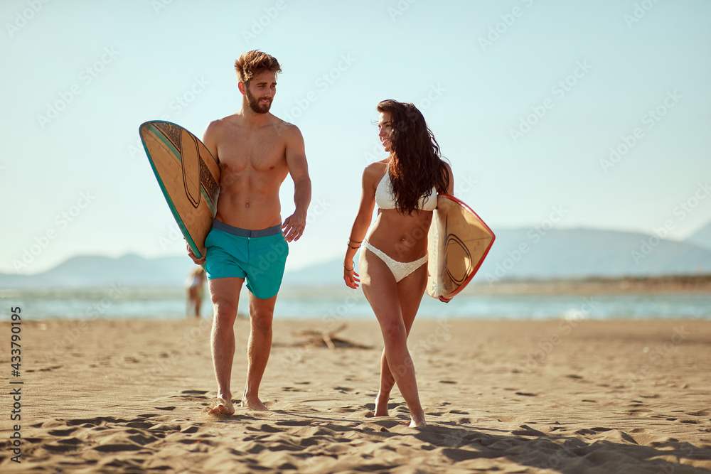 Young couple of surfers is enjoying hot sun while walking the beach at sea. Summer, vacation, sea, together
