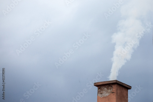 Selective blur on a smoking chimney rejecting white fume brick on the roof of an individual residential house exhausting little fumes at dusk, during a cloudy afternoon...