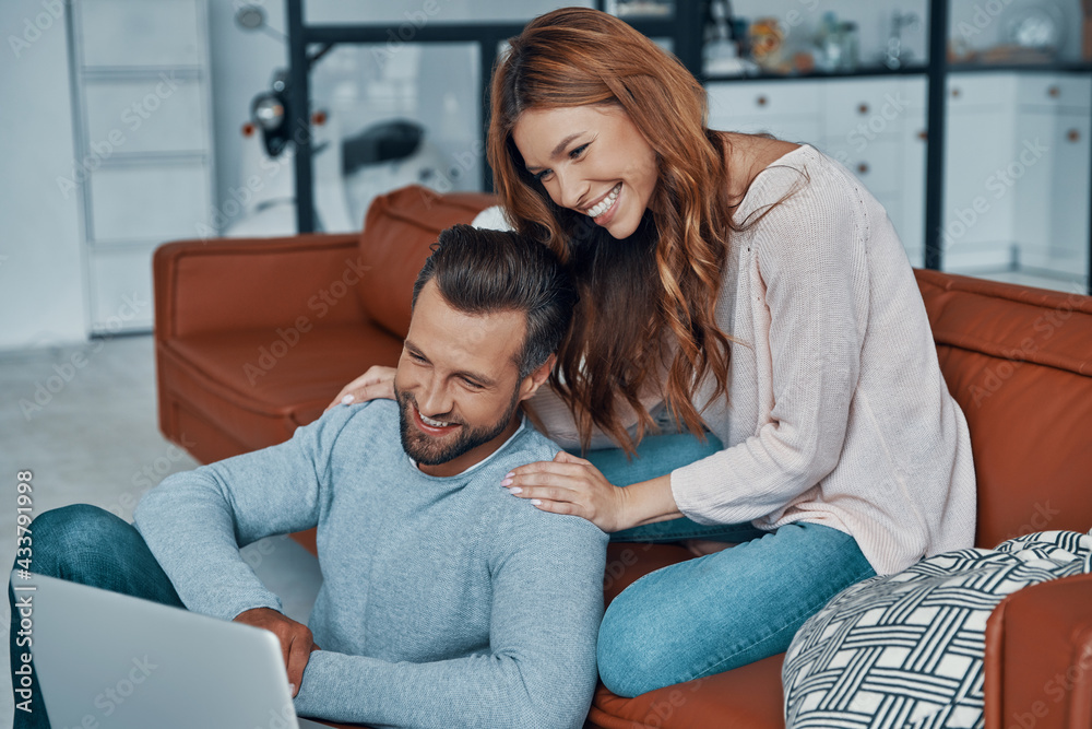 Happy young couple using laptop and smiling while spending time at home