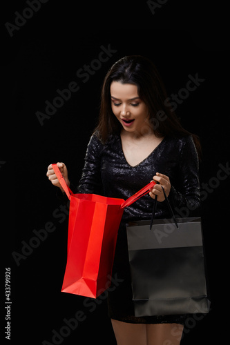 a young woman in a black dress is happy with a gift, shopping in black and red bags. on a black isolated background
