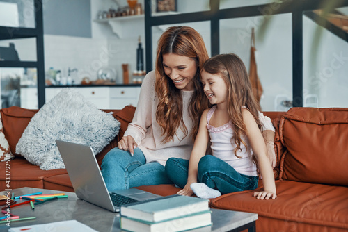 Fotografi Mother and her daughter bonding together and smiling while using laptop at home