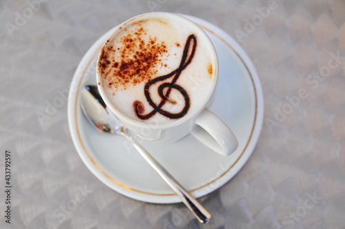 Cup of coffee latte cappuccino with cream, cacao powder and treble clef made from chocolate