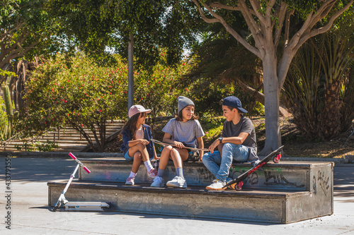 Three skating kids, sitting in a skate park talking and laughing together.