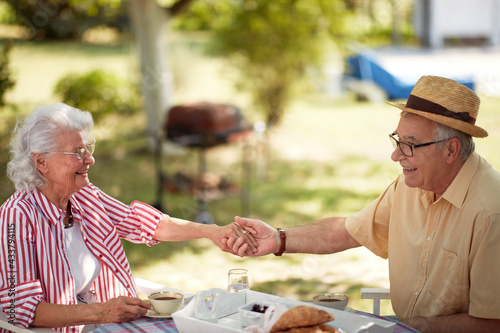 cute caucasian elderly couple enjoy outdoor, having breakfast and coffee, holding hands