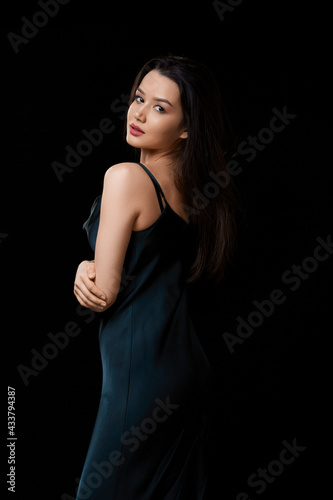 young woman in dark blue dress . on a black isolated background.she touches her face with her hand. it stands half-turned.