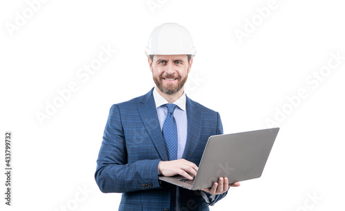 happy man in suit and safety helmet wotking on computer online isolated on white, agile business. © Olena