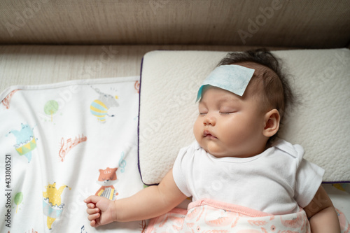 asian baby infant get fever and apply cool patch on forehead sleeping at home after vaccination. cold pad gel healing temperature. baby sick after back from hospital. photo