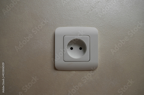 Electrical socket isolated on gray wall. Renovated studio apartment power supply background. Empty copy space single white plastic power outlet.
