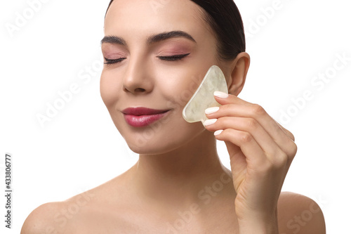 Beautiful young woman doing facial massage with gua sha tool on white background, closeup