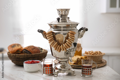 Traditional Russian samovar with treats on white table in kitchen