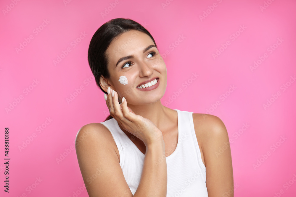 Young woman applying facial cream on pink background Young woman applying facial cream on pink background