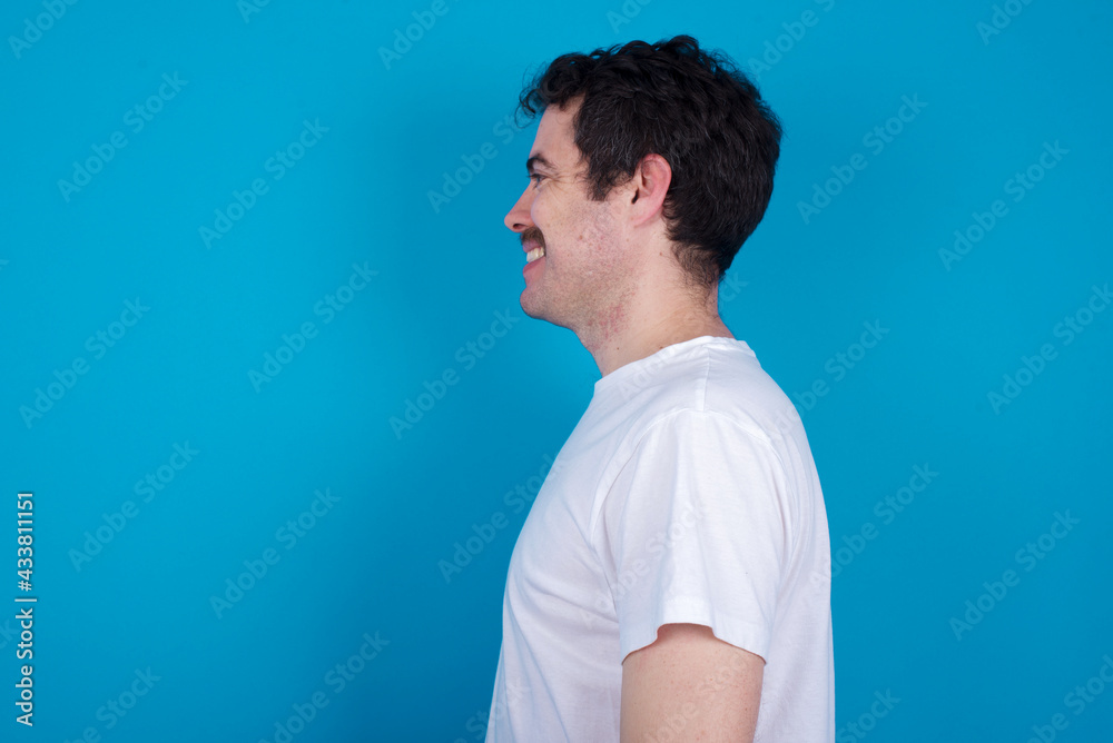 Profile portrait of nice young handsome Caucasian man with moustache wearing white t-shirt against white background look empty space toothy smile Profile portrait of nice young handsome Caucasian man with moustache wearing white t-shirt against white background look empty space toothy smile
