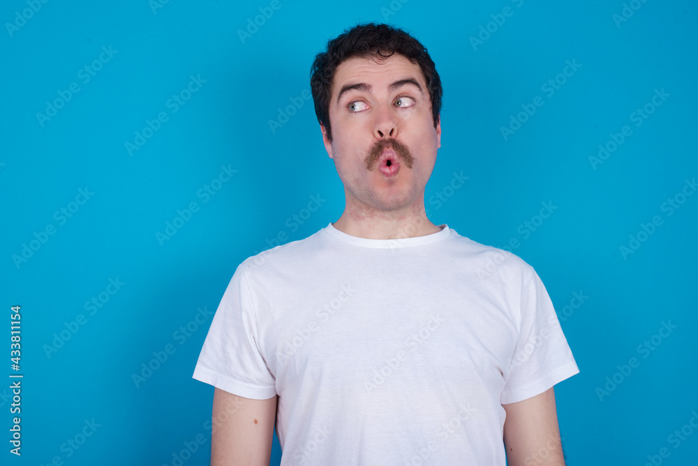 Fototapeta premium Shocked young handsome Caucasian man with moustache wearing white t-shirt against white background look empty space with open mouth screaming: Oh My God! I can't believe this.