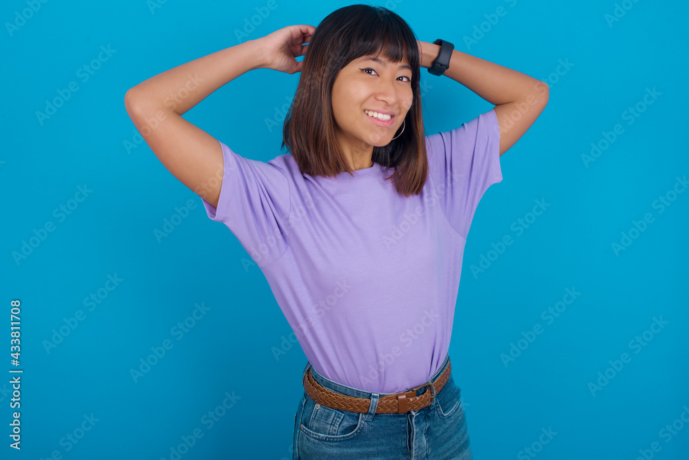 Young beautiful asian girl wearing purple t-shirt against blue background stretching arms, relaxed position. Young beautiful asian girl wearing purple t-shirt against blue background stretching arms, relaxed position.