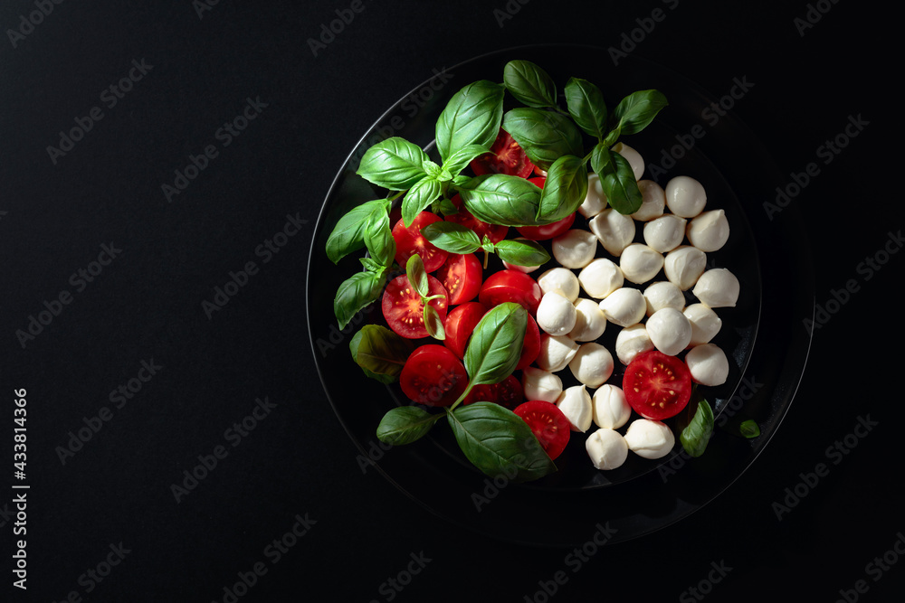 Caprese salad with tomato, mini mozzarella and basil on a black plate. Caprese salad with tomato, mini mozzarella and basil on a black plate.