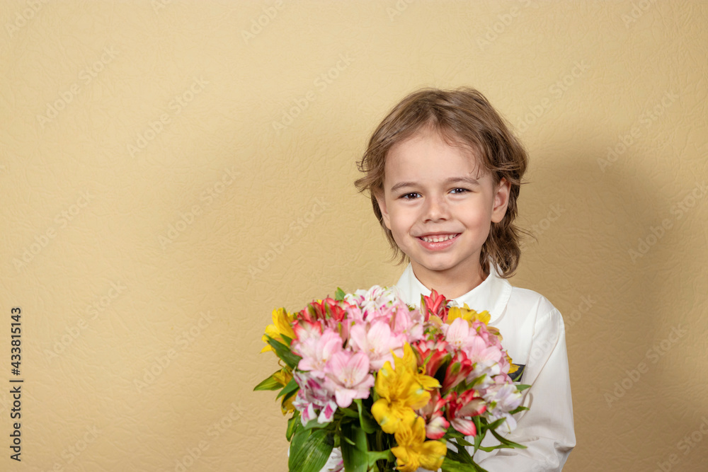 smiling handsome boy holds out a bouquet of colorful flowers on yellow background. happy child gives a bouquet of multicolored alstroemeria. smiling handsome boy holds out a bouquet of colorful flowers on yellow background. happy child gives a bouquet of multicolored alstroemeria.