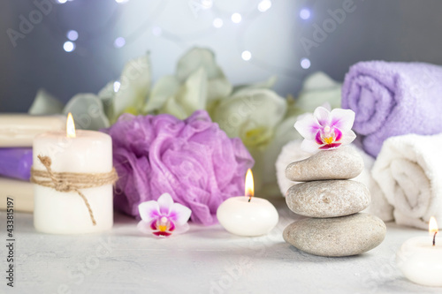 massage stones, burning candles, rolled towels, flowers, abstract lights. Spa resort therapy composition in lilac colors