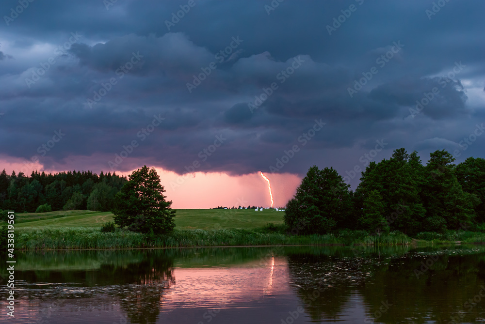 Beautiful dramatic thunderstorm sunset with dark rainy clouds and lightning over the lake.