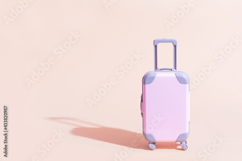Pink Suitcase toy on a peach, sandy background. Minimalism and travel concept