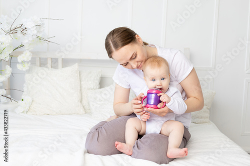 mom drinks or bottle feeds a baby on a white bed at home, baby food concept