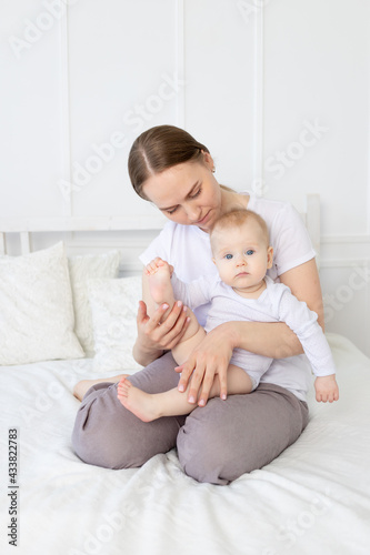 an anxious mother with a baby in her arms holds the baby's leg on the bed at home