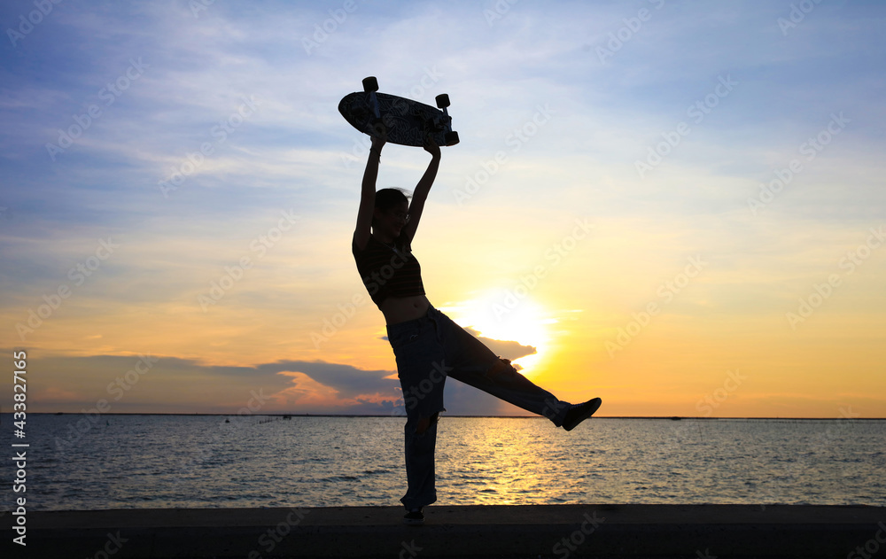 Happy and funny Young woman play surf board or surf skate board on bridge along seashore aginst sunset