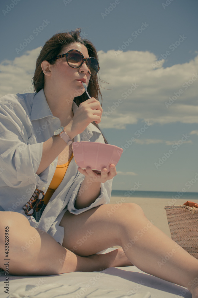 Young Caucasian girl having a good time on a sunny summer beach day while she eats a variety of fruits. Summer concept 2021. Summer Concept 2021.