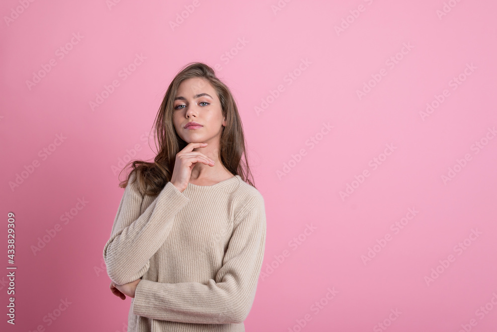a young attractive girl holds her chin in her hand, a position of pride and arrogance. portrait of a young woman on a pink background copy space