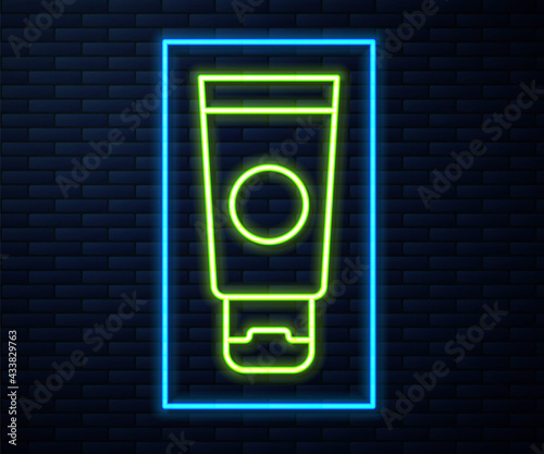 Glowing neon line Cream or lotion cosmetic tube icon isolated on brick wall background. Body care products for men. Vector