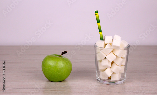 Healthy food versus unhealthy sugary high-calorie drinks. Sugar cubes in a glass with a straw and a green apple photo