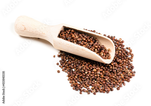 wood scoop on grains of paradise pepper on white