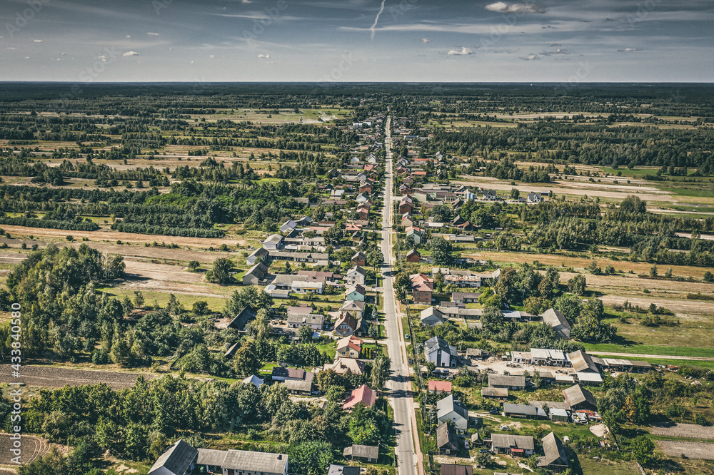 Fototapeta premium Aerial view of village surrounded by agricultural fields under blue sky idyllic view