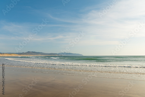 Blue transparent sky with lacy white clouds over the ocean. Mountains can be seen in the distance. Pastel shades. Beautiful nature. There is an empty space for your signature.