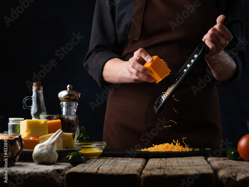 Pizza making process. Chef grates cheese. On a rough wooden table, ingredients for pizza - garlic, soy sauce, lemons, zucchini. Vegetarian food. Bright paint products and dark background