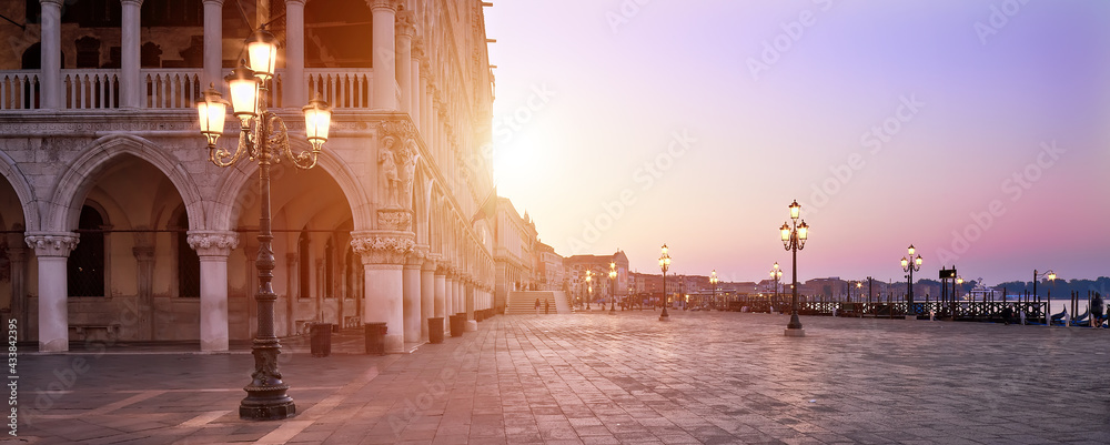 Banner, San Marco square at sunrise early in the morning. Venice or Venezia city, Italy, Europe. Panoramic composition, illuminated architecture, image toned orange. Sunrise, sun flare.