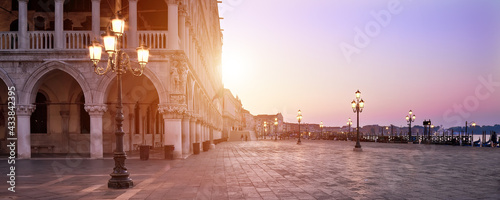 Banner, San Marco square at sunrise early in the morning. Venice or Venezia city, Italy, Europe. Panoramic composition, illuminated architecture, image toned orange. Sunrise, sun flare. © tilialucida