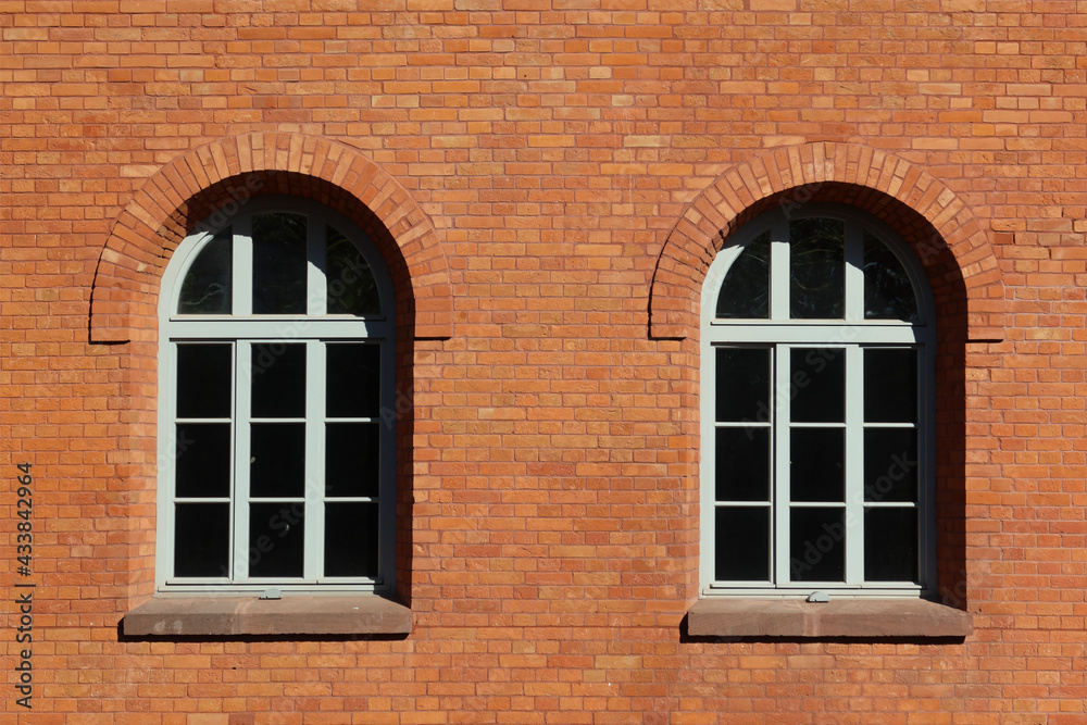 Two arched glass windows set in red brick wall building