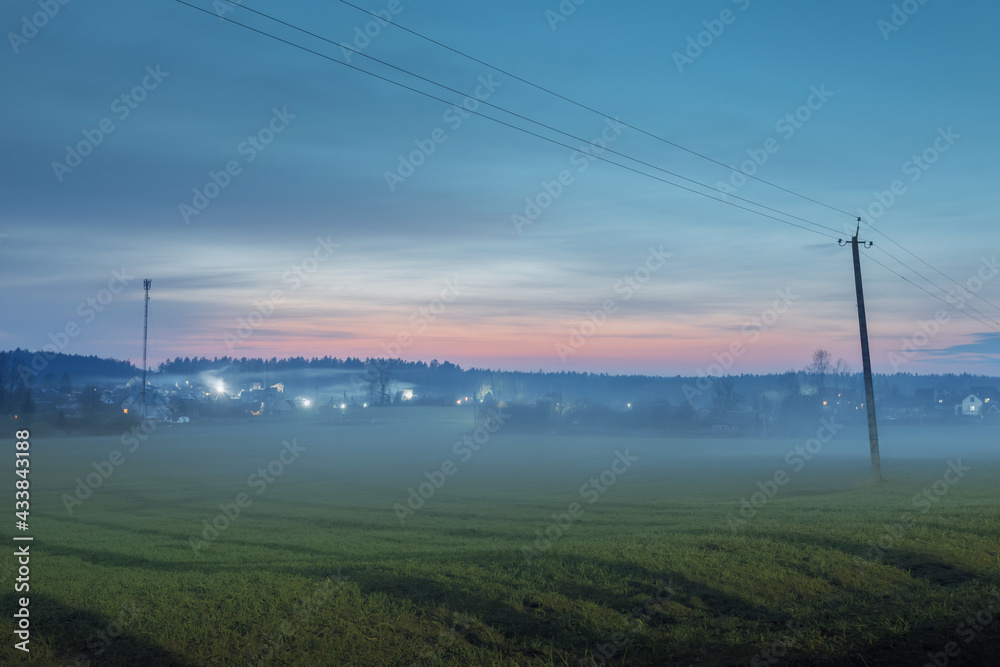 Field and lonely houses in the distance in the spring before dawn in the fog