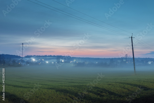 Field and lonely houses in the distance in the spring before dawn in the fog