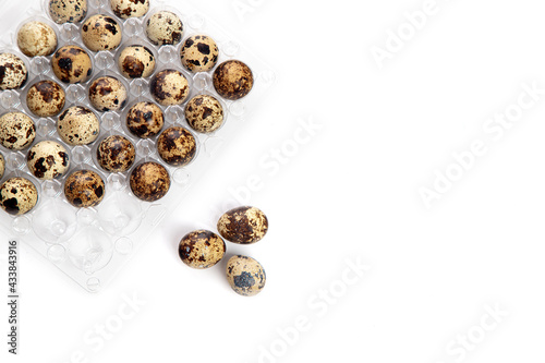Quail eggs in a transparent plastic container. Three eggs lie side by side on a white background. Top view