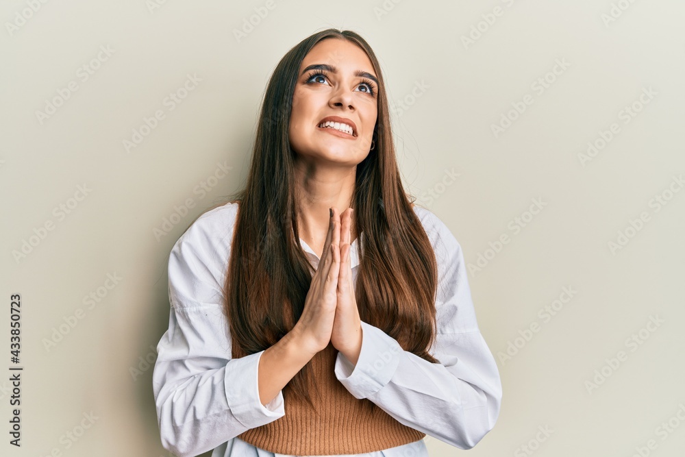 Beautiful brunette young woman wearing casual clothes begging and praying with hands together with hope expression on face very emotional and worried. begging. Beautiful brunette young woman wearing casual clothes begging and praying with hands together with hope expression on face very emotional and worried. begging.