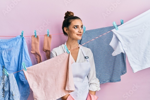 Beautiful brunette young woman washing clothes at clothesline smiling looking to the side and staring away thinking.
