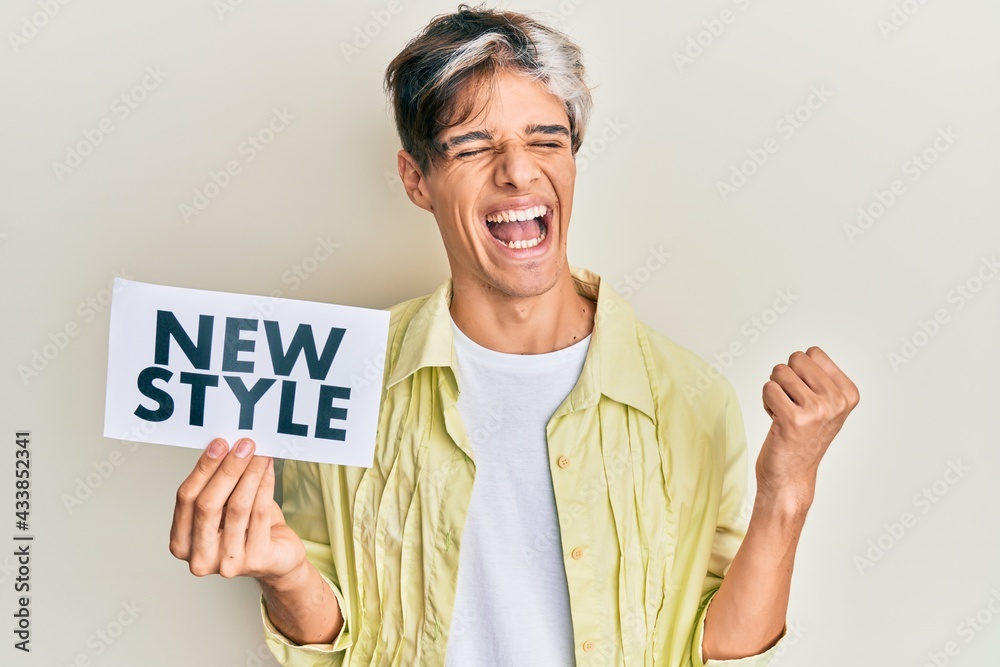 Young hispanic man holding new style message on paper screaming proud, celebrating victory and success very excited with raised arm Young hispanic man holding new style message on paper screaming proud, celebrating victory and success very excited with raised arm