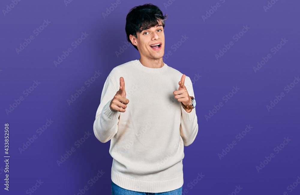 Handsome hipster young man wearing casual winter sweater pointing fingers to camera with happy and funny face. good energy and vibes.