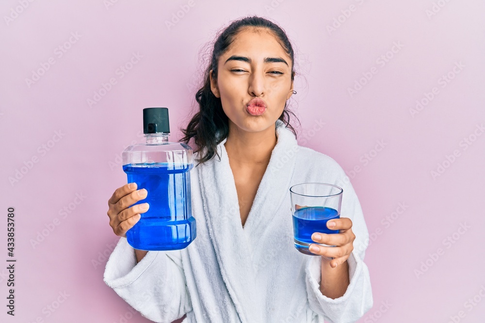 Hispanic teenager girl with dental braces holding mouthwash looking at the camera blowing a kiss being lovely and sexy. love expression. Hispanic teenager girl with dental braces holding mouthwash looking at the camera blowing a kiss being lovely and sexy. love expression.