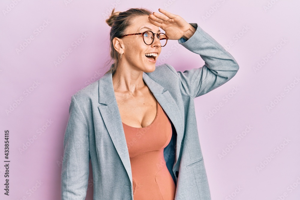Beautiful caucasian woman wearing business jacket and glasses very happy and smiling looking far away with hand over head. searching concept. Beautiful caucasian woman wearing business jacket and glasses very happy and smiling looking far away with hand over head. searching concept.