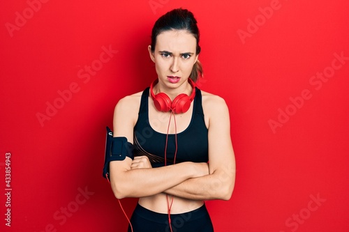 Young hispanic girl wearing gym clothes and using headphones skeptic and nervous, disapproving expression on face with crossed arms. negative person.