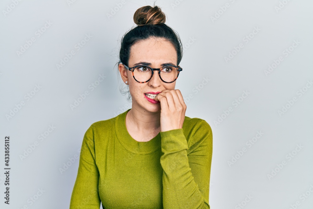 Young hispanic girl wearing casual clothes and glasses looking stressed and nervous with hands on mouth biting nails. anxiety problem. Young hispanic girl wearing casual clothes and glasses looking stressed and nervous with hands on mouth biting nails. anxiety problem.